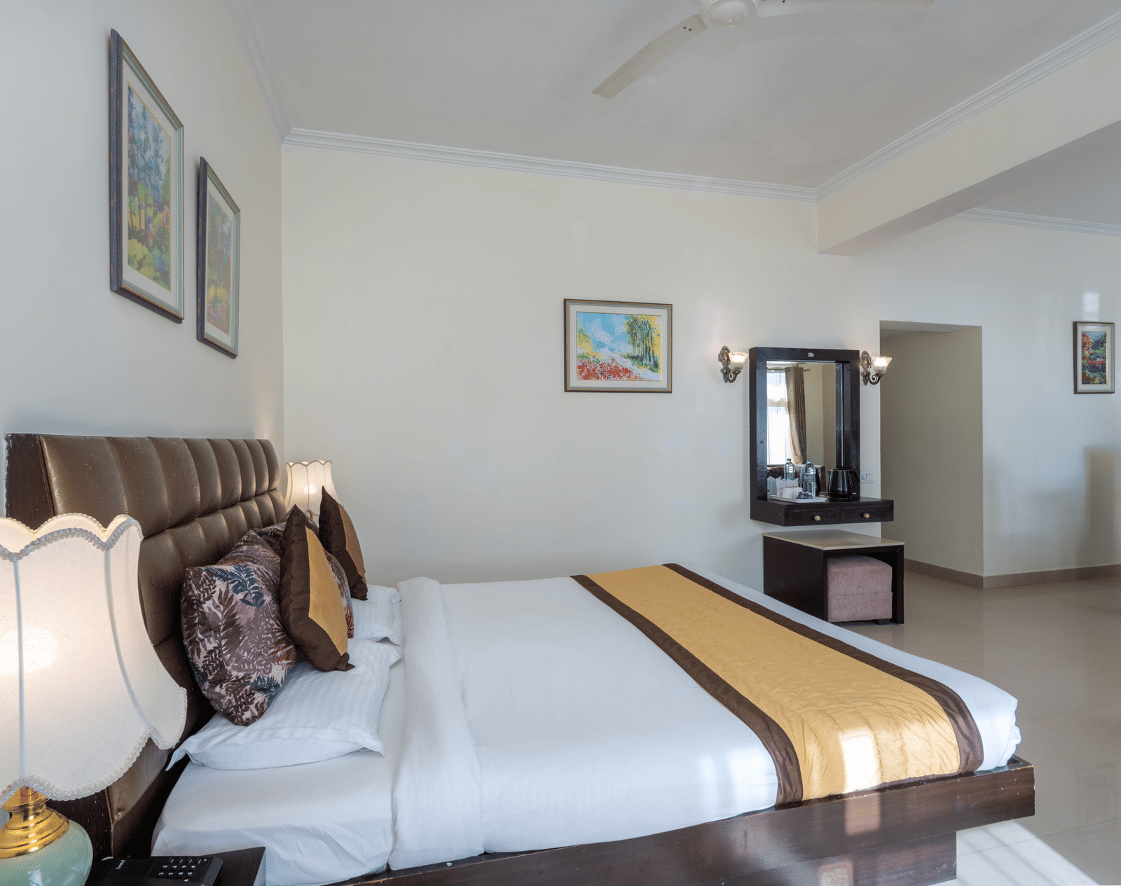 A spacious hotel room with a large bed, a dresser with a mirror, a lamp, and artwork on the walls | DLS The Pearl